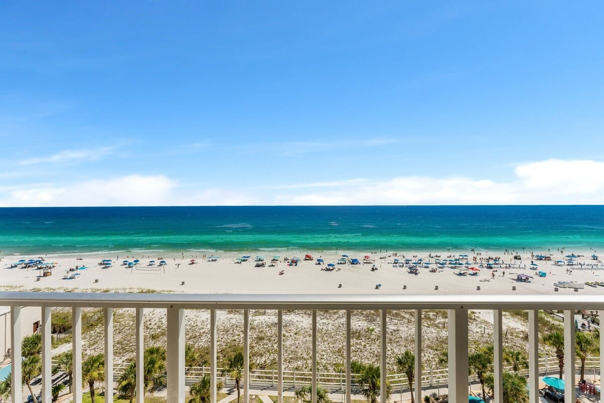 The Summit 927 – View from balcony overlooking beach with umbrellas, palm trees, and ocean under blue sky.