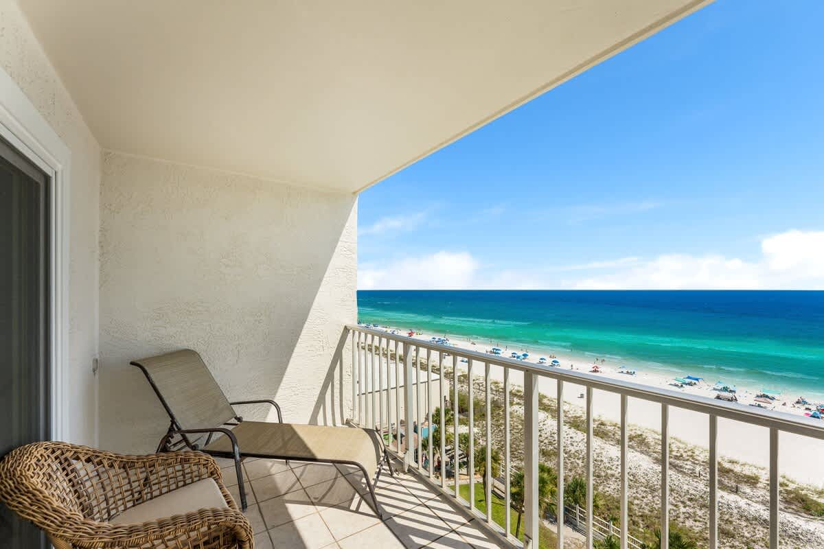 The Summit 927 – Balcony view of beach and ocean, with a lounge chair and woven chair.