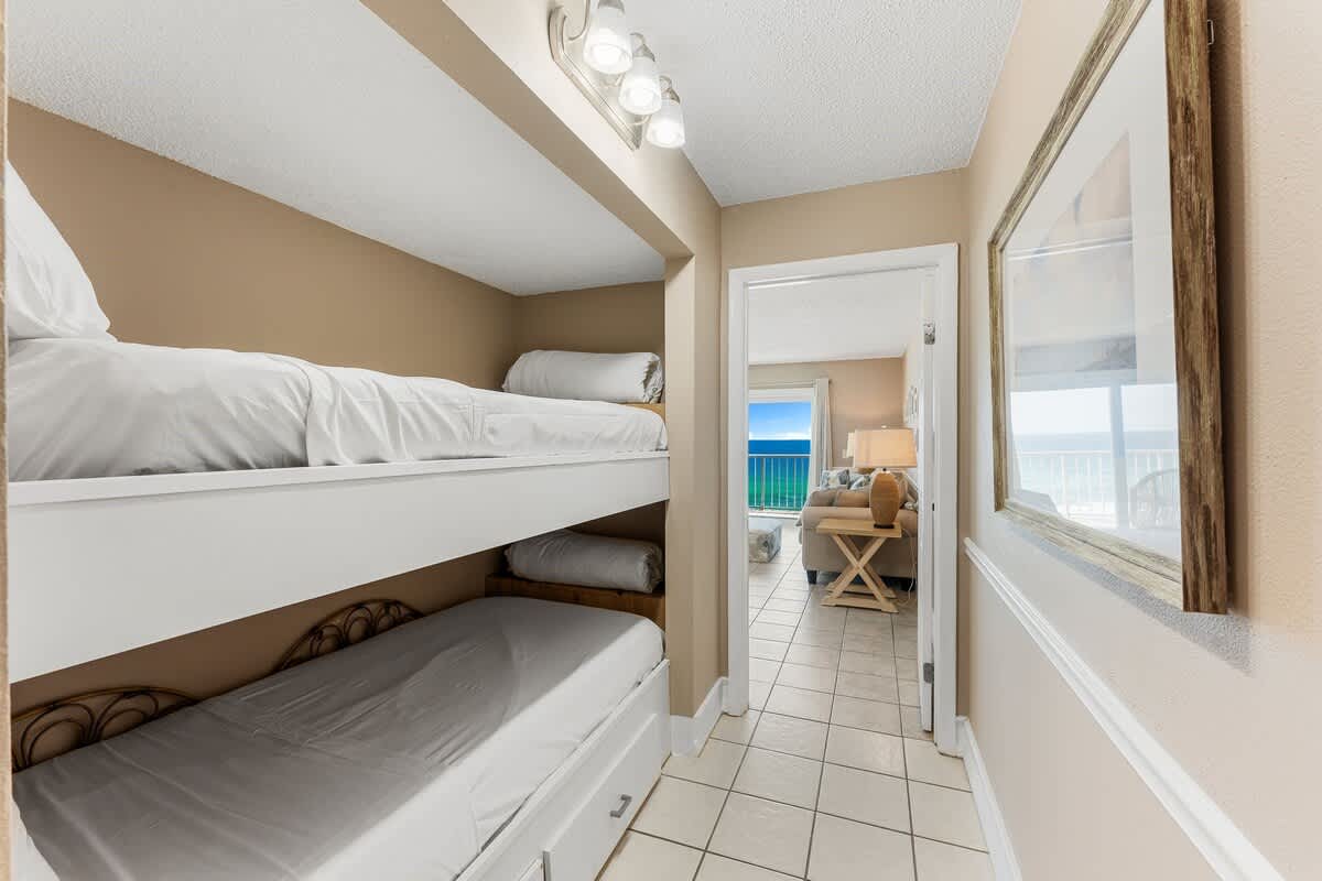 The Summit 927 – Bunk beds in a hallway leading to a living area with ocean view, light-colored decor, and tile flooring.