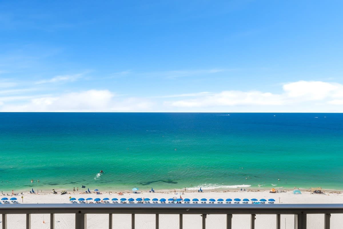 The Summit 1001 – View of the beach with umbrellas and clear blue water from a balcony.
