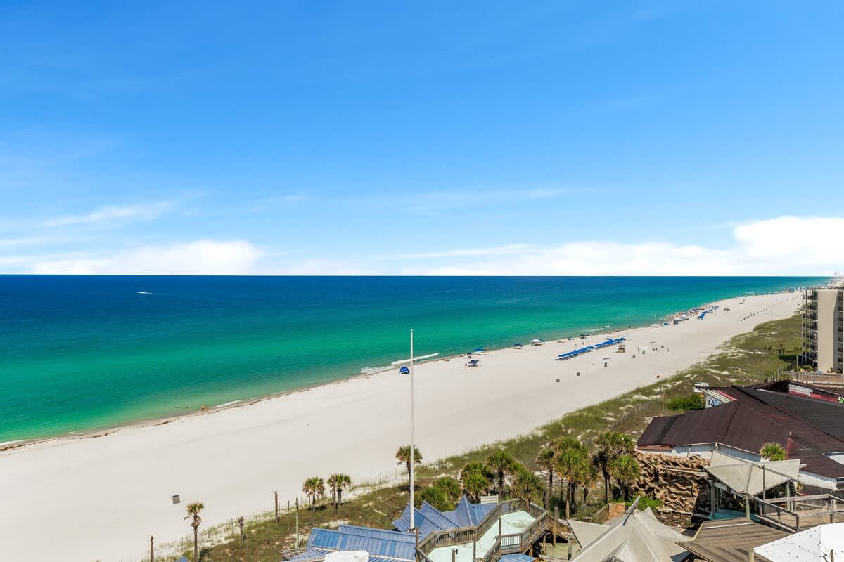 The Summit 1001 – Beachfront view with white sand, clear blue water, and a few beachgoers in the distance.