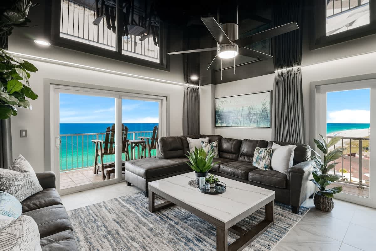 The Summit 1001 – Living room with large sectional sofa, ocean view, balcony with seating, potted plants, and modern decor.