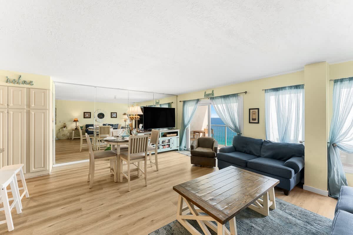 The Summit 1502 – Living room with a sofa, dining area, and ocean view through glass doors.