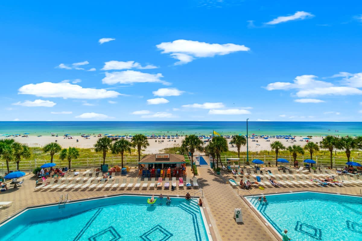 The Summit 1502 – Pool area with lounge chairs and beach view, featuring palm trees and umbrellas.