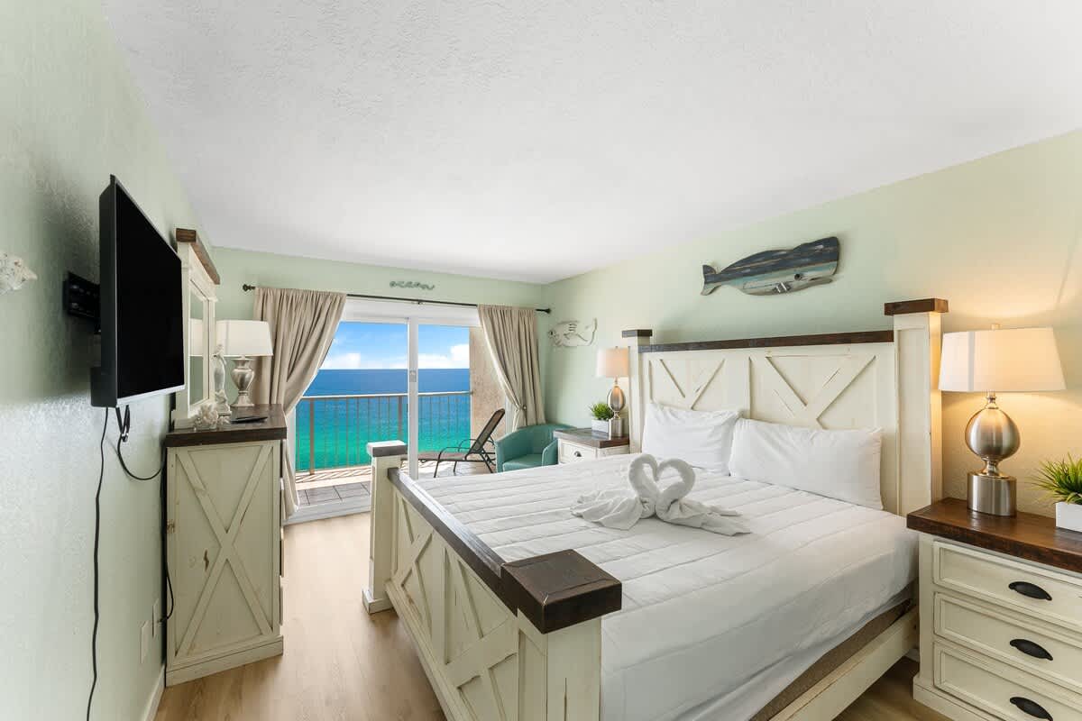 The Summit 1502 – Cozy bedroom with a king-size bed, coastal decor, and ocean view through large sliding glass doors.