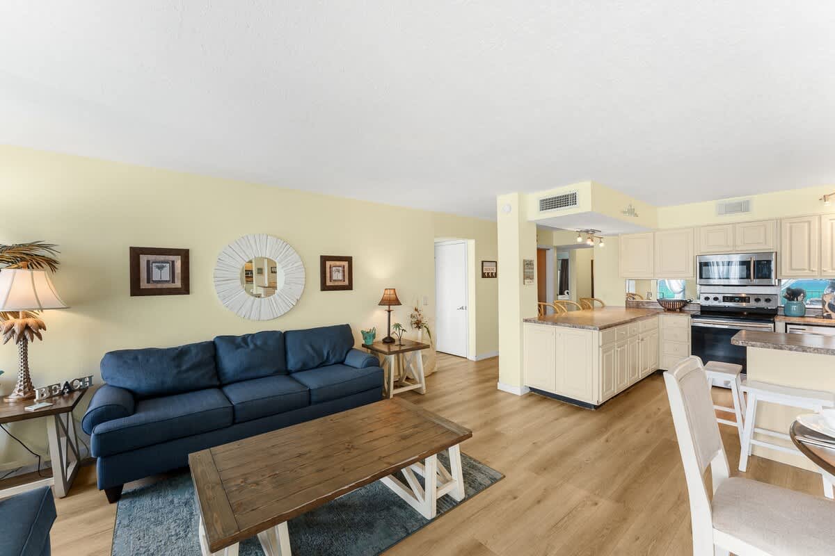 The Summit 1502 – Living room with blue sofa, wooden coffee table, open kitchen, and light-colored walls.