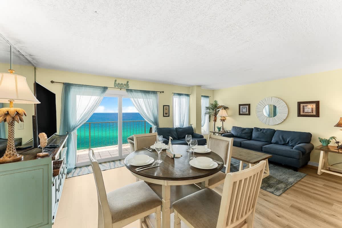 The Summit 1502 – Living room with ocean view, dining table, two blue sofas, and light-colored walls.
