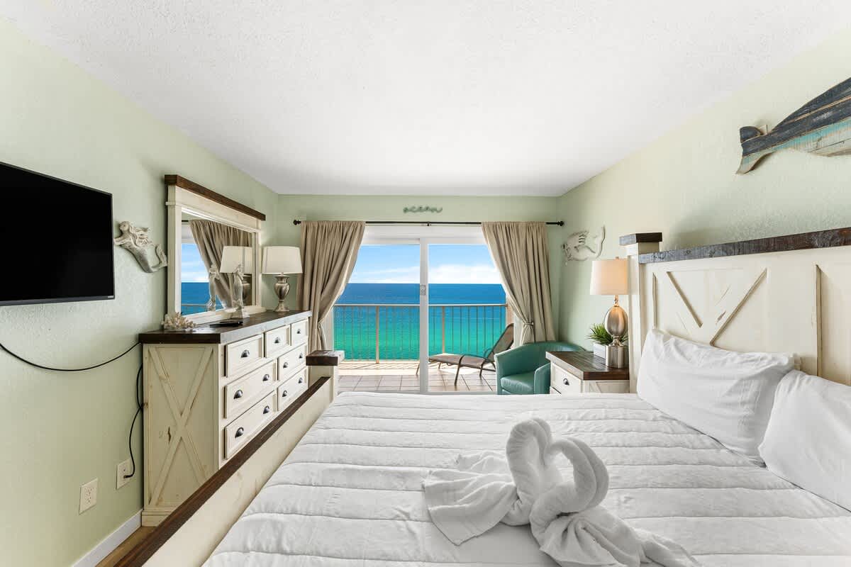 The Summit 1502 – Bedroom with a king bed, dresser, balcony view of the ocean, and a seating area.