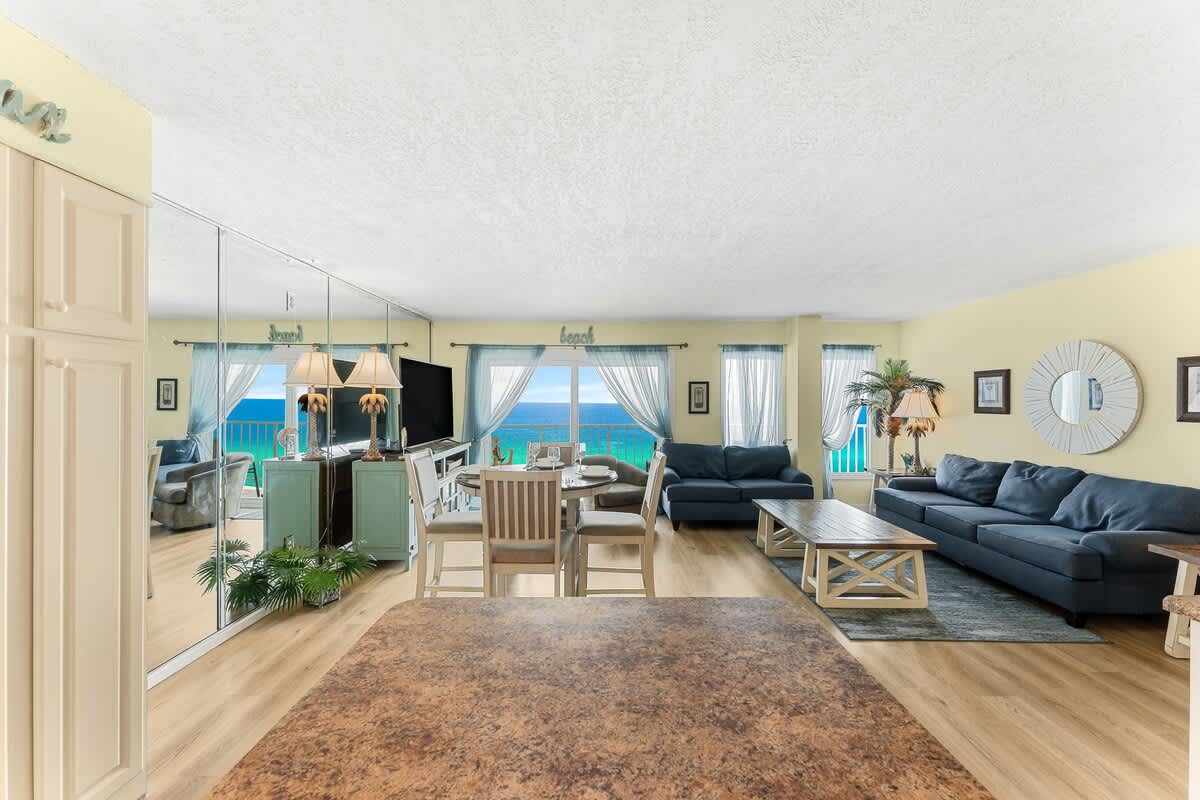The Summit 1502 – Living room with ocean view, blue sofas, dining table, and large windows.