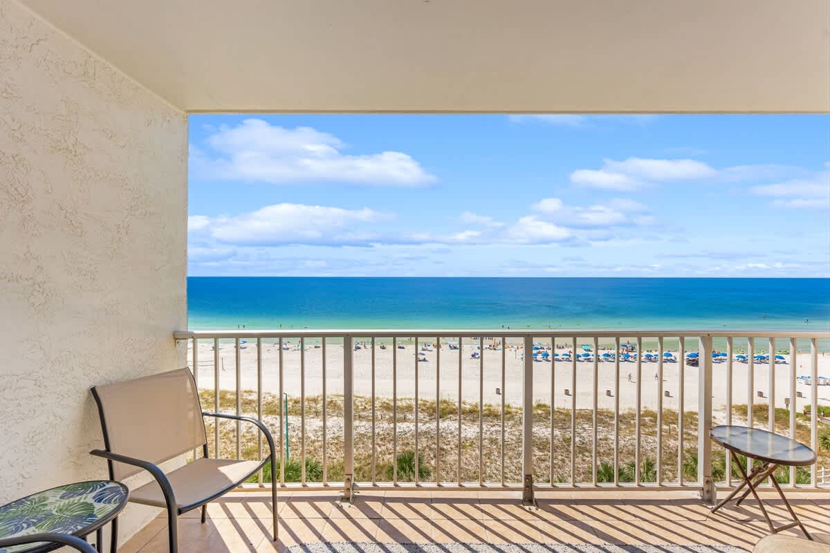 The Summit 828 – Balcony view overlooking sandy beach and ocean, featuring two chairs and a small table.