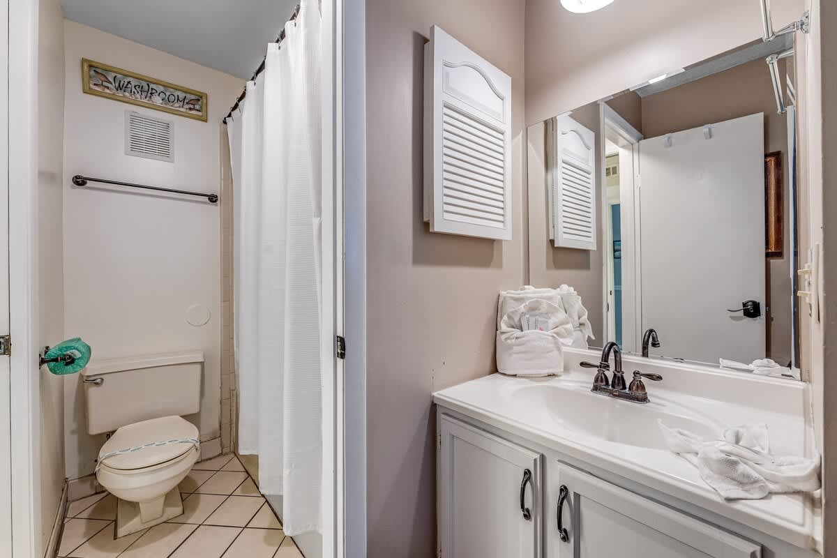 The Summit 828 – Bathroom with a toilet, sink, mirror, and shower curtain. Towels neatly arranged on the countertop.