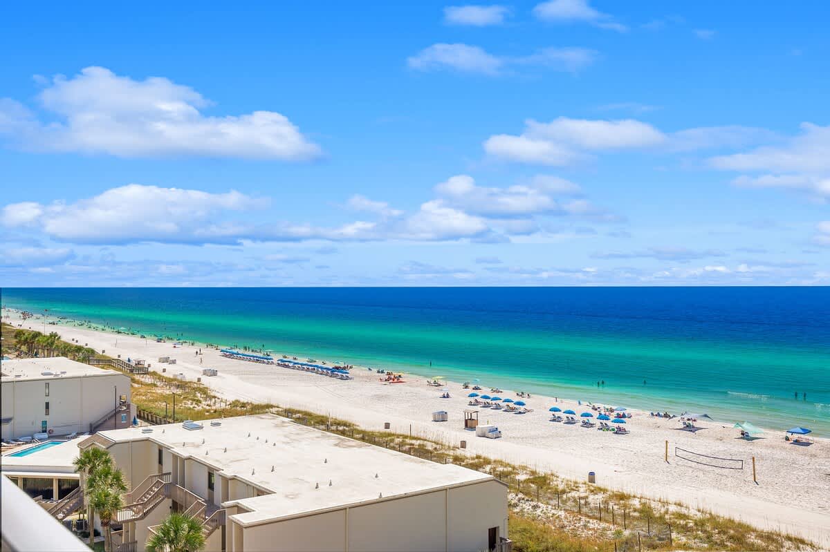 The Summit 828 – Ocean view from balcony overlooking sandy beach and beach chairs under blue sky.