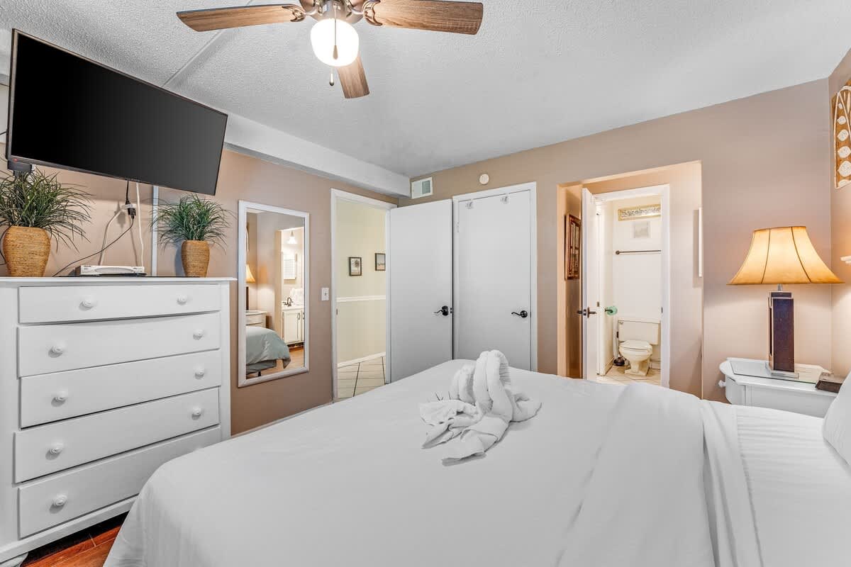 The Summit 828 – Bedroom featuring a bed with white linens, a dresser, TV, and connected bathroom entry.