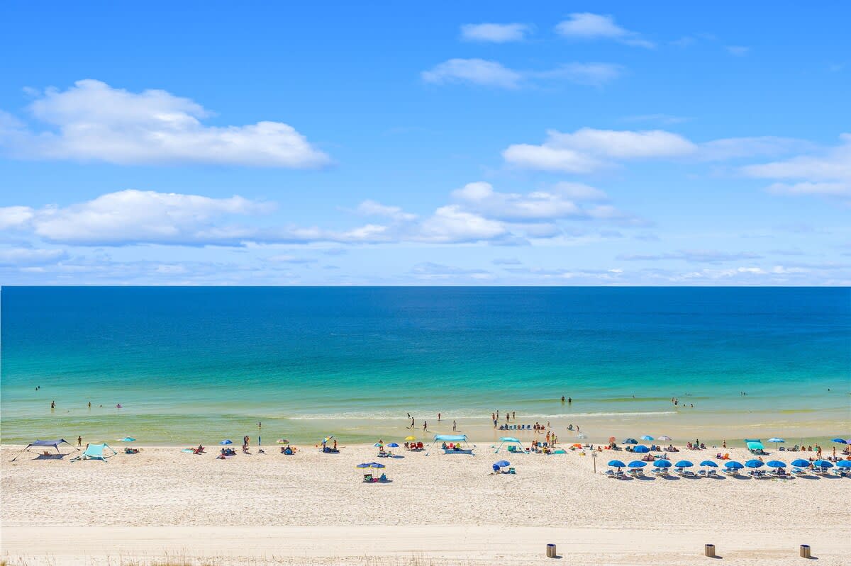The Summit 828 – View of a beach with umbrellas, people swimming, and a clear blue sky.