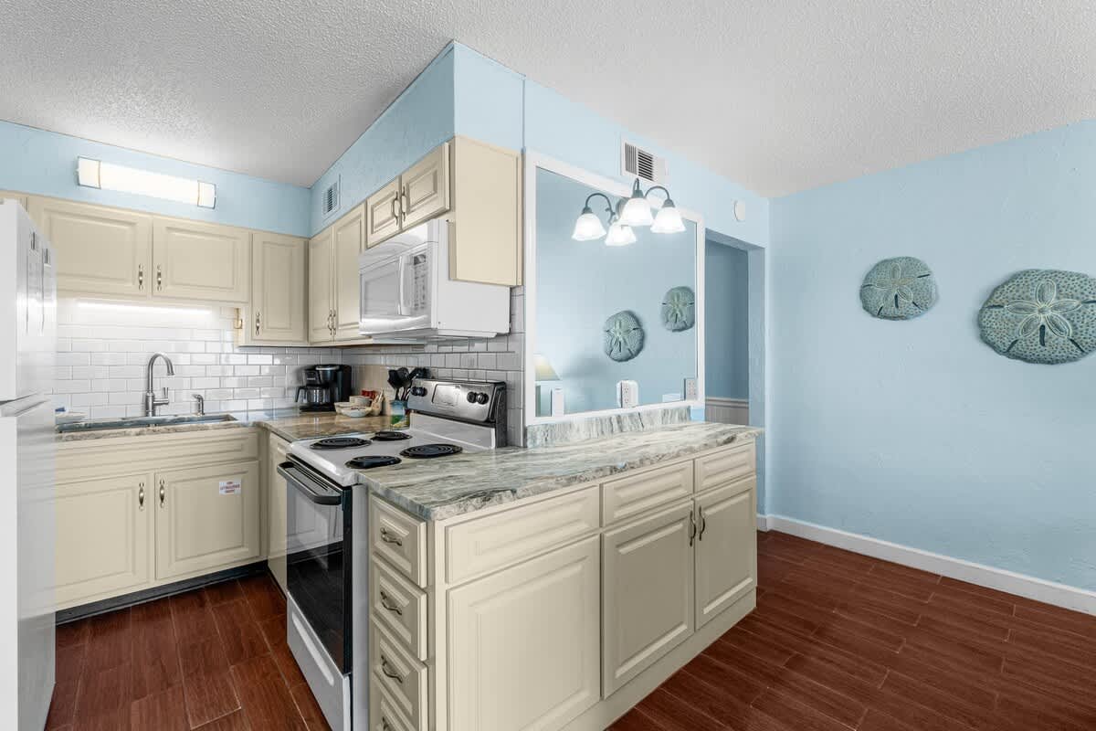The Summit 408 – Bright kitchen with light blue walls, granite counters, white appliances, and decorative wall art.