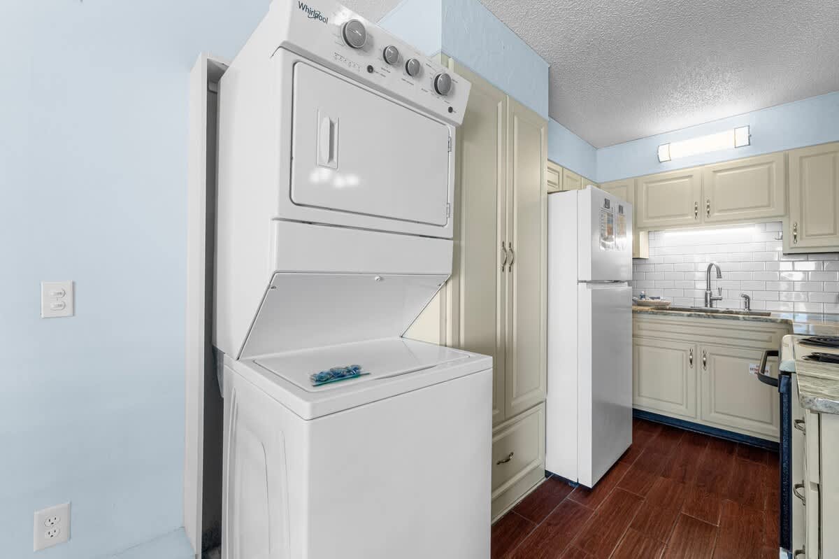 The Summit 408 – Stacked washer and dryer near a kitchen with white cabinets and appliances, wood flooring, and a backsplash.