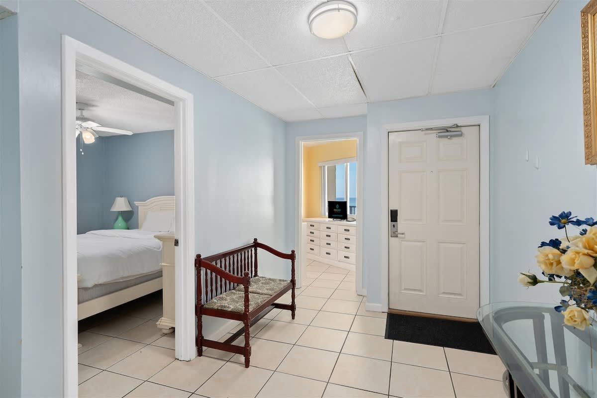 Moondrifter 606 – Hallway with tiled floor, a bench, and views of a bedroom and beachfront through a window.