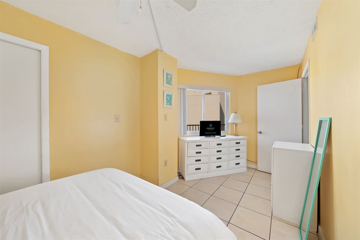 Moondrifter 606 – Bedroom with yellow walls, dresser, TV, and window, featuring a view of a building.