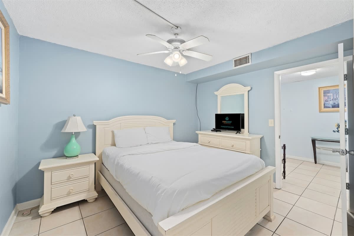 Moondrifter 606 – Bedroom with a queen bed, light blue walls, ceiling fan, dresser, and adjoining room view.
