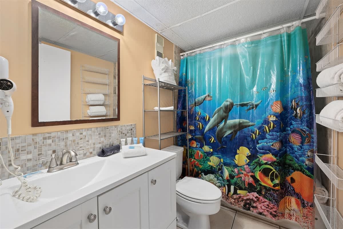 Moondrifter 606 – Bathroom with colorful underwater-themed shower curtain, vanity sink, and shelving for towels.