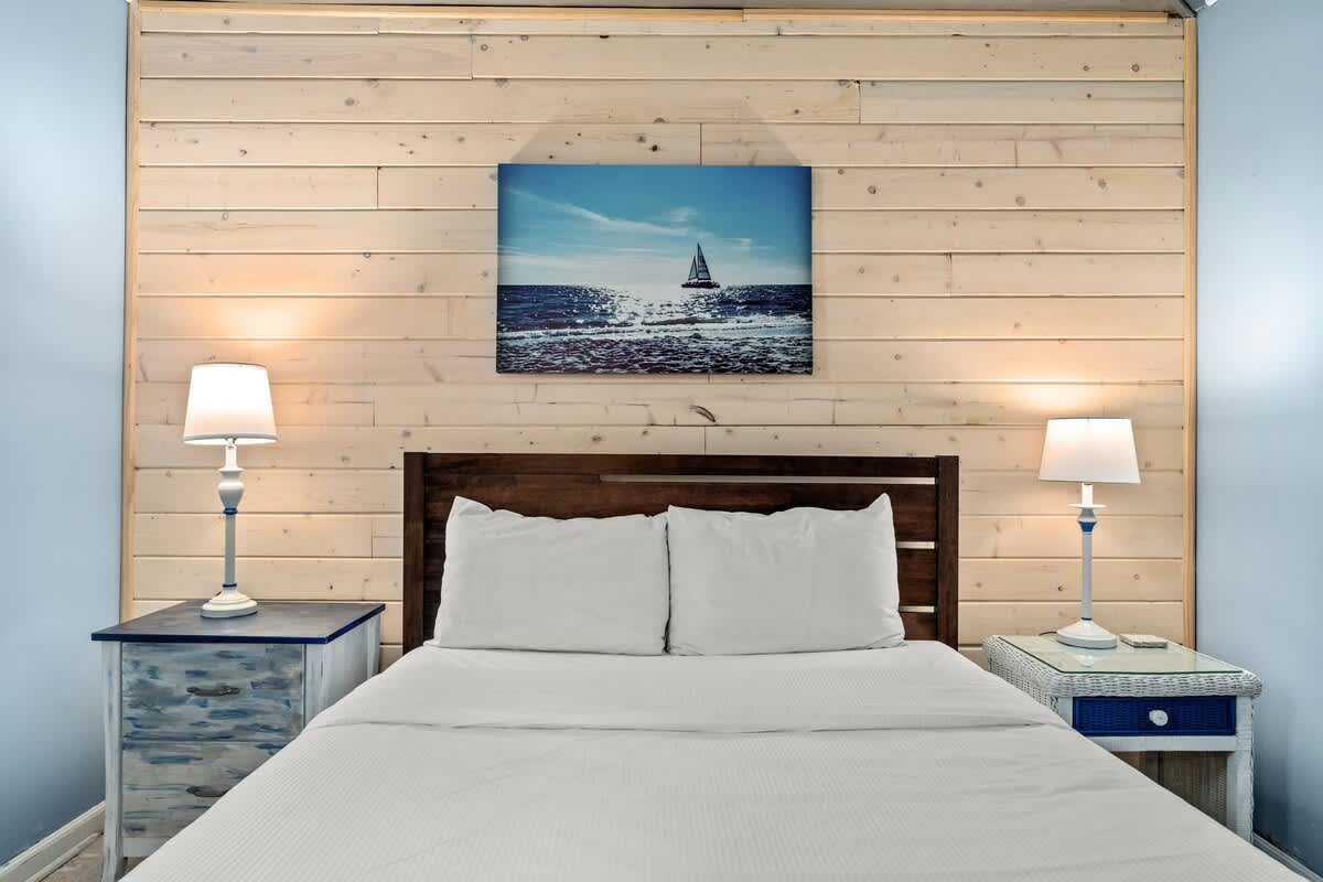 Sunbird 811E – Cozy bedroom with a wooden headboard, two lamps, and a painting of a sailboat on the wall.