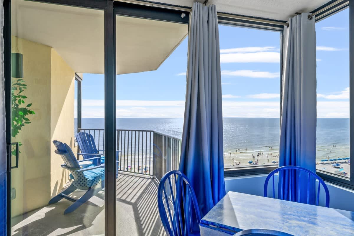Sunbird 811E – Coastal view from a dining area featuring blue chairs, a table, and a balcony with two lounge chairs.