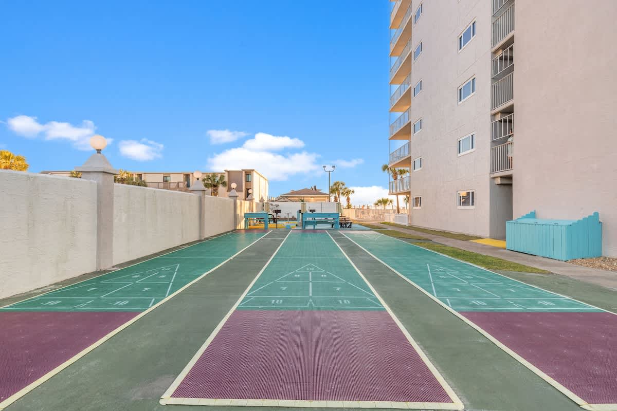 The Summit 524 – Shuffleboard court with benches and palm trees in background, adjacent to a multi-story building.