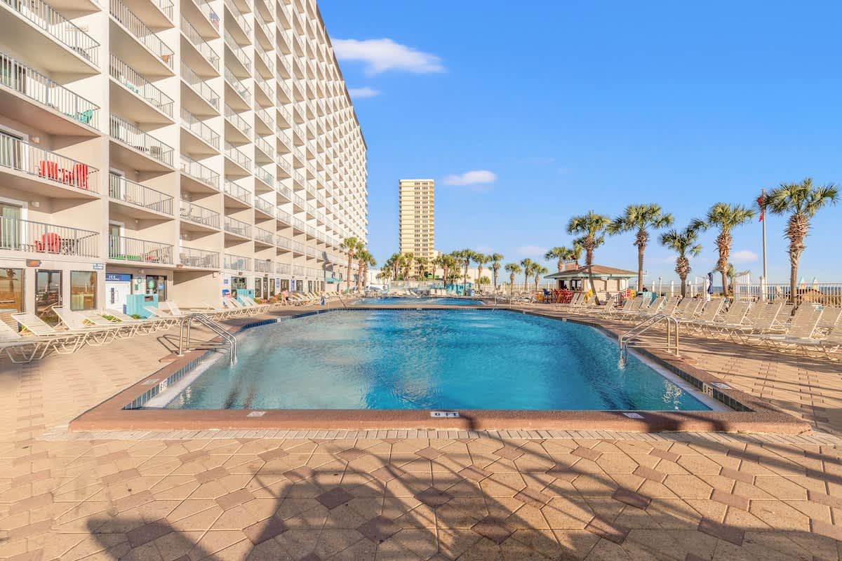 The Summit 524 – Outdoor pool surrounded by lounge chairs and palm trees, with a multi-story building in the background.