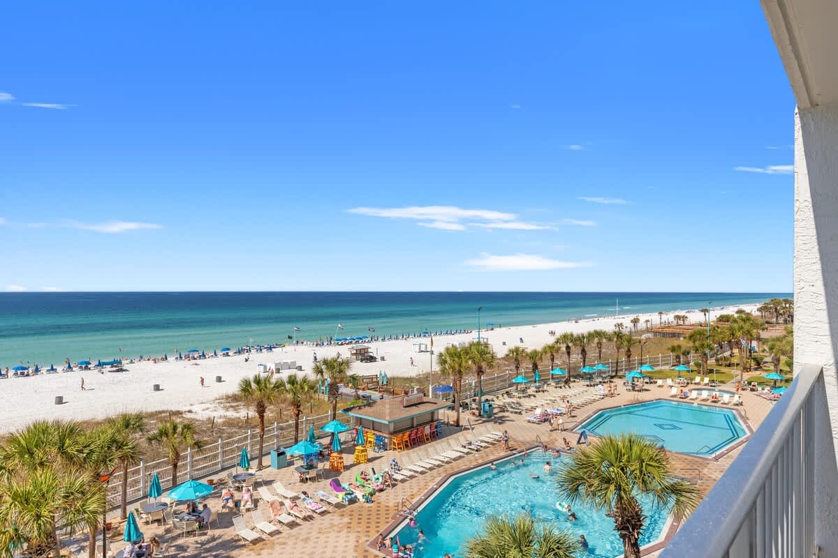 The Summit 524 – View from balcony showing pool, beach, and ocean with palm trees and umbrellas.