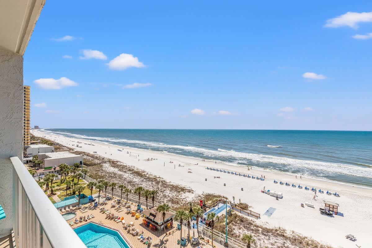 The Summit 524 – Ocean view from balcony overlooking a beach, pool area, and palm trees.