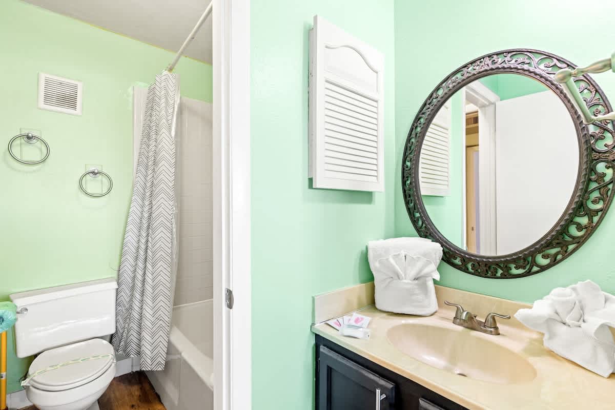 The Summit 524 – Bathroom with green walls, shower curtain, sink, mirror, and folded towels.