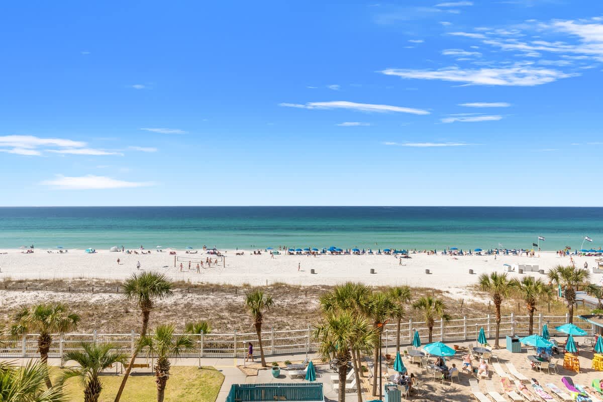 The Summit 524 – View of a white sand beach, ocean, and palm trees from a balcony.