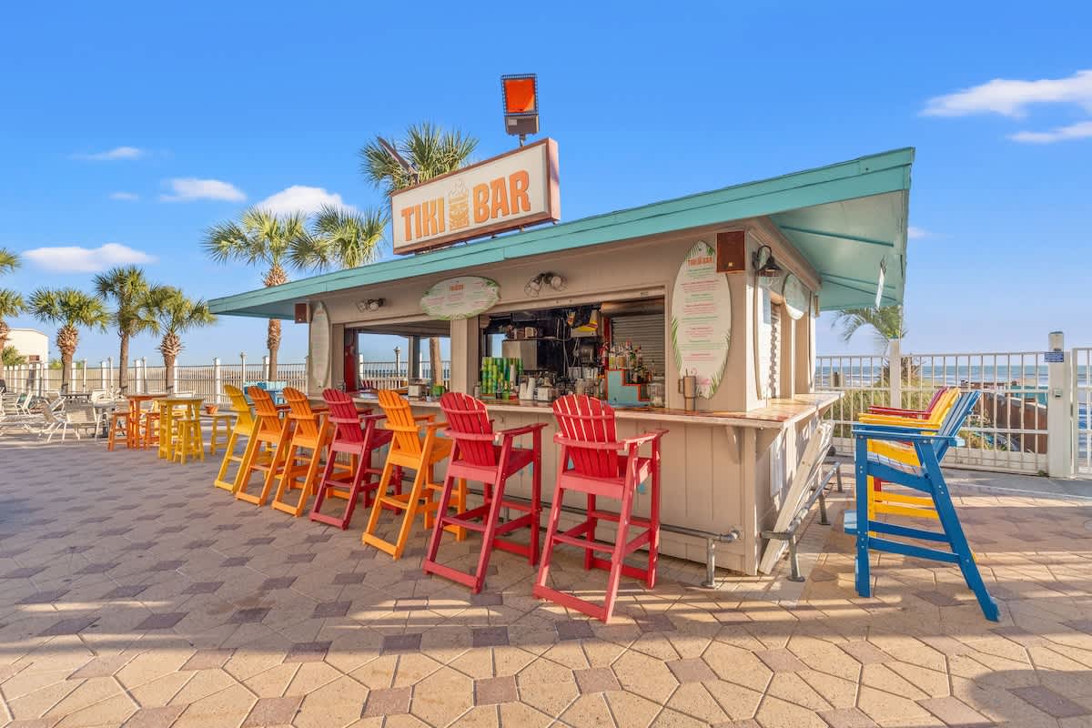 The Summit 524 – Outdoor tiki bar with colorful stools, surrounded by palm trees and a view of the ocean.
