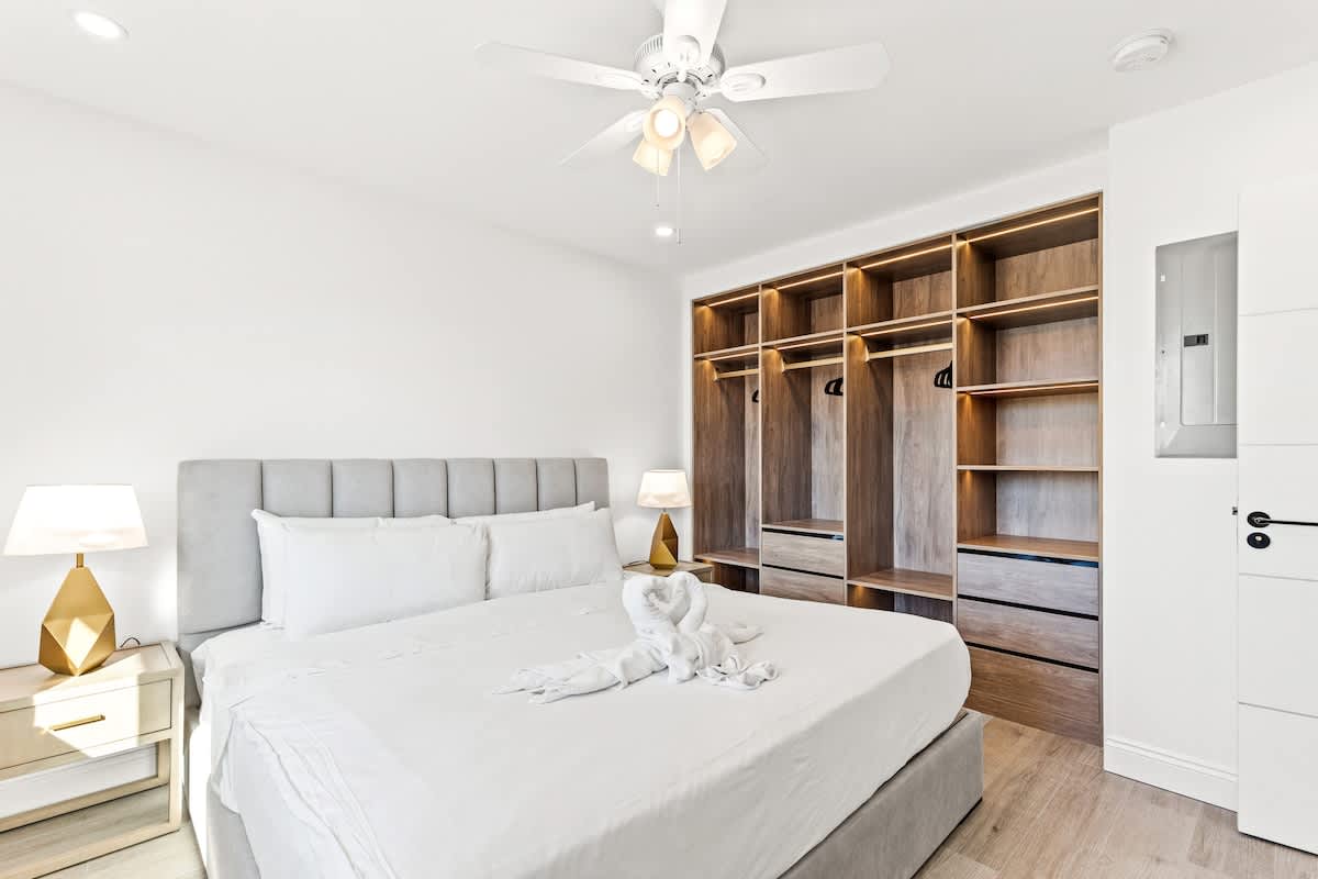 Ocean Breeze 1D – Bright bedroom with a queen bed, ceiling fan, and built-in closet shelving.
