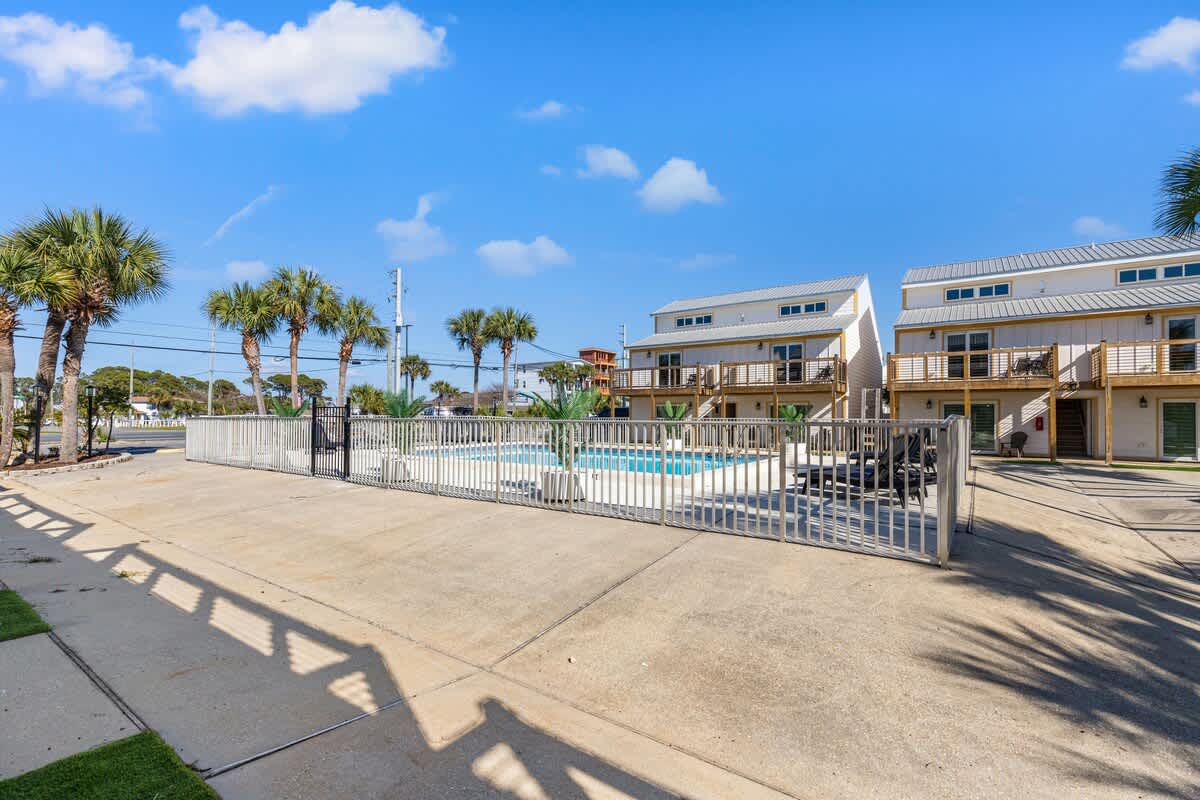 Ocean Breeze 2A – Concrete area with pool, palm trees, and two-story vacation rental buildings in the background.