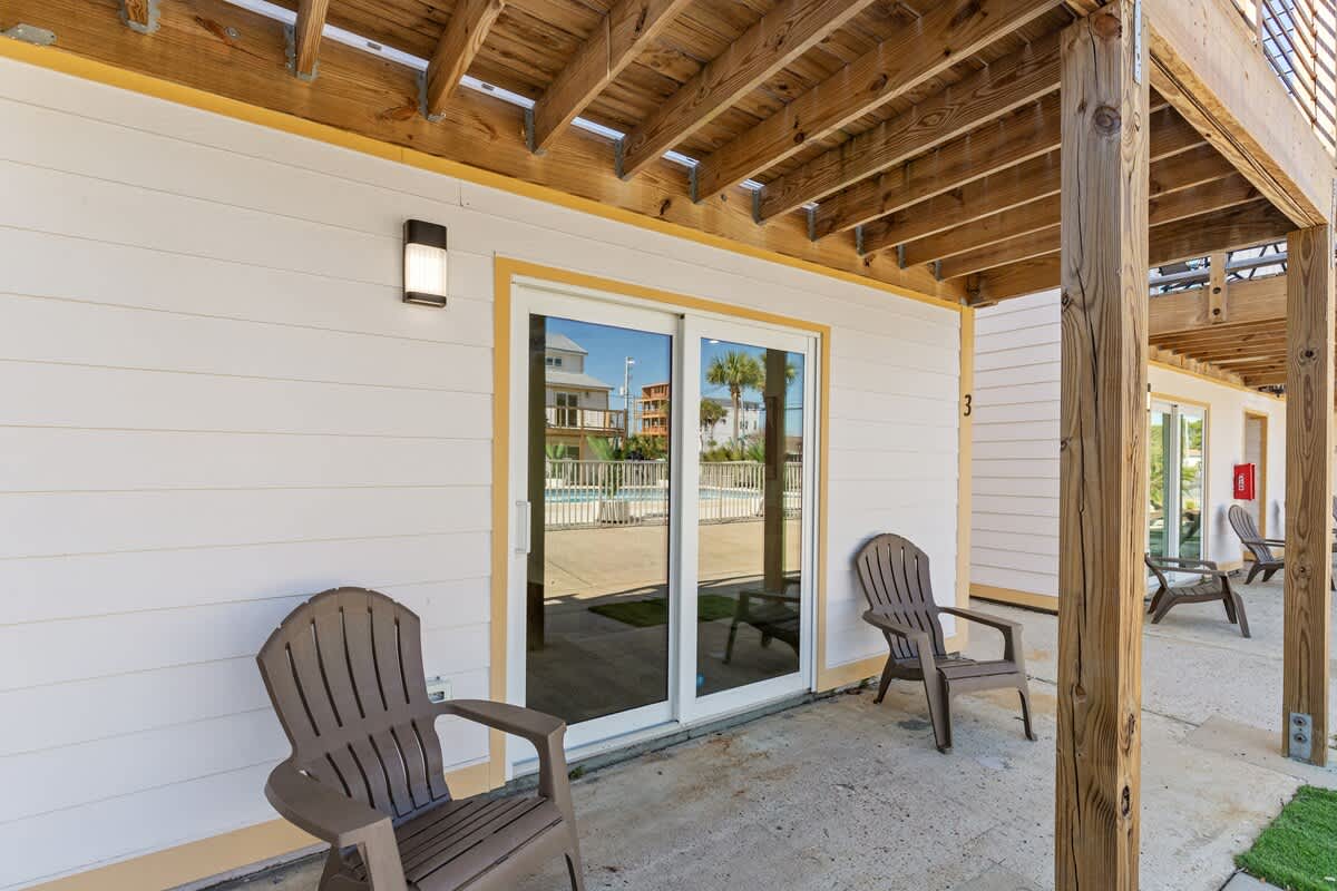 Ocean Breeze 2A – Ground-level vacation rental with two chairs, sliding door, and view of a pool area.