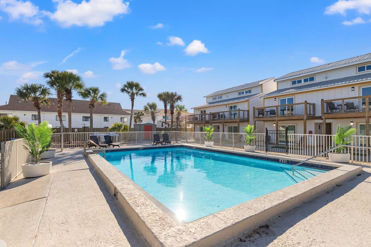 Ocean Breeze 2C – Swimming pool surrounded by palm trees and lounge chairs, with vacation rental buildings in the background.