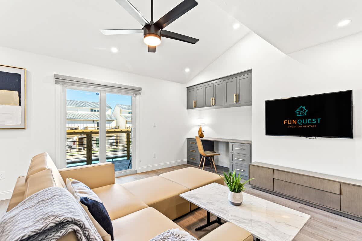Ocean Breeze 2C – Living room with beige sectional sofa, marble coffee table, desk area, and sliding glass door to balcony view.
