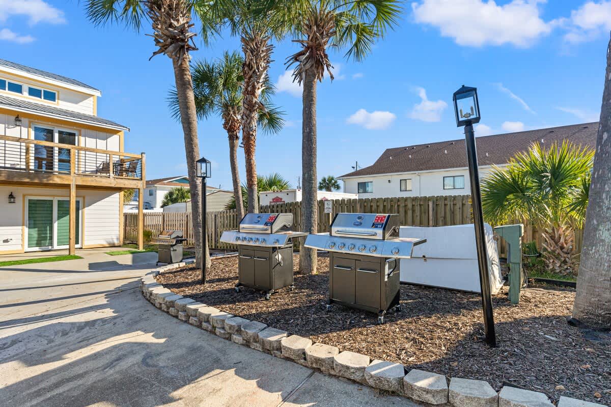 Ocean Breeze 2C – Outdoor area with two grills, palm trees, and a view of adjacent buildings.