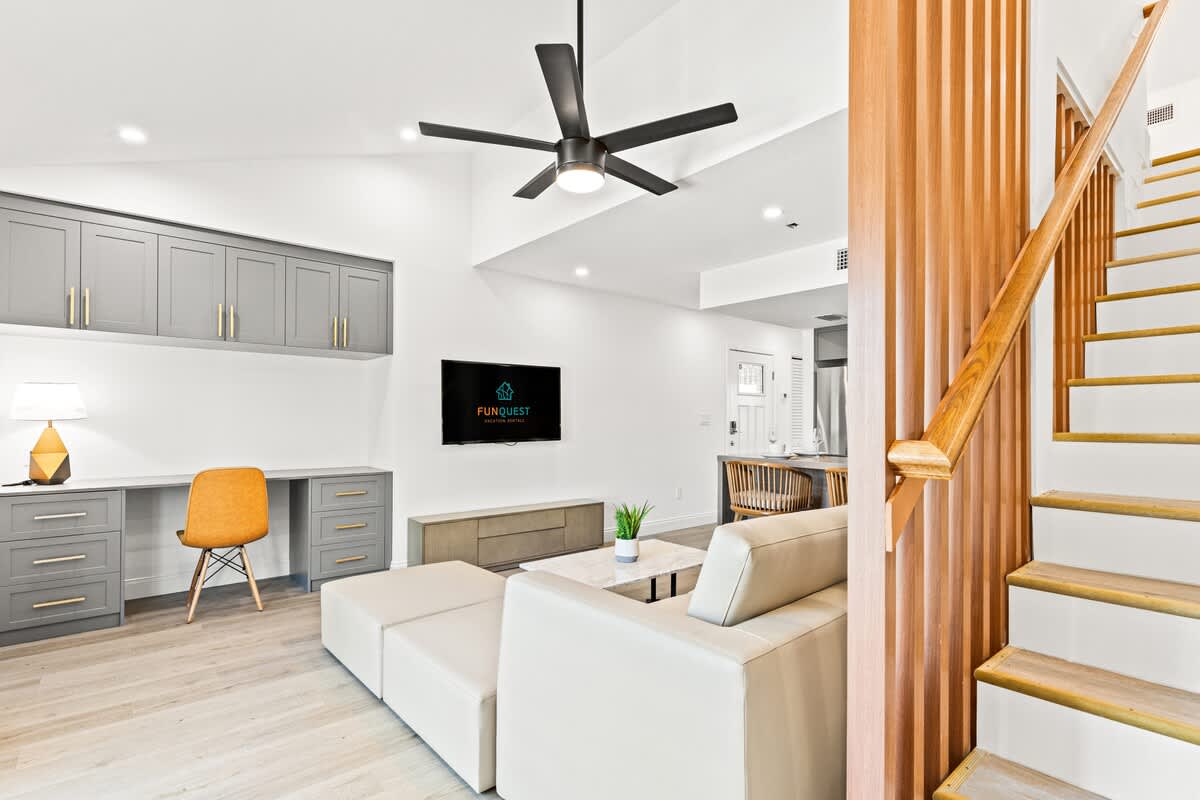 Ocean Breeze 2C – Bright living room with a sectional sofa, desk, wall-mounted TV, and staircase to upper level.