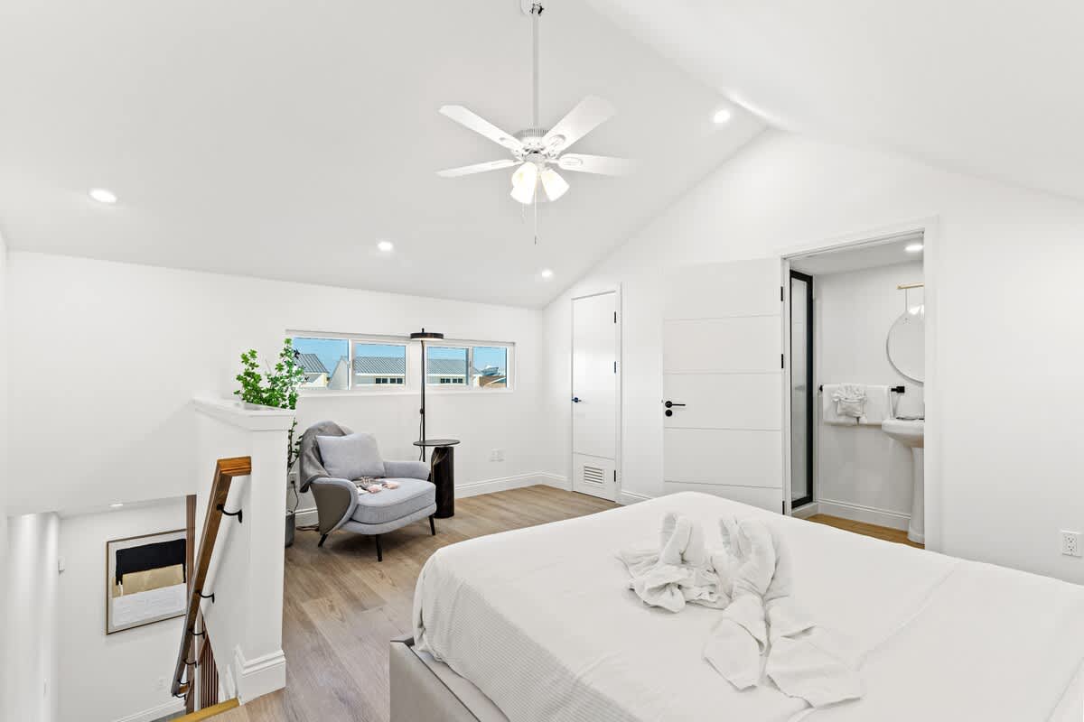 Ocean Breeze 2C – Bright bedroom with a king bed, armchair, and en-suite bathroom, featuring large windows with a view.