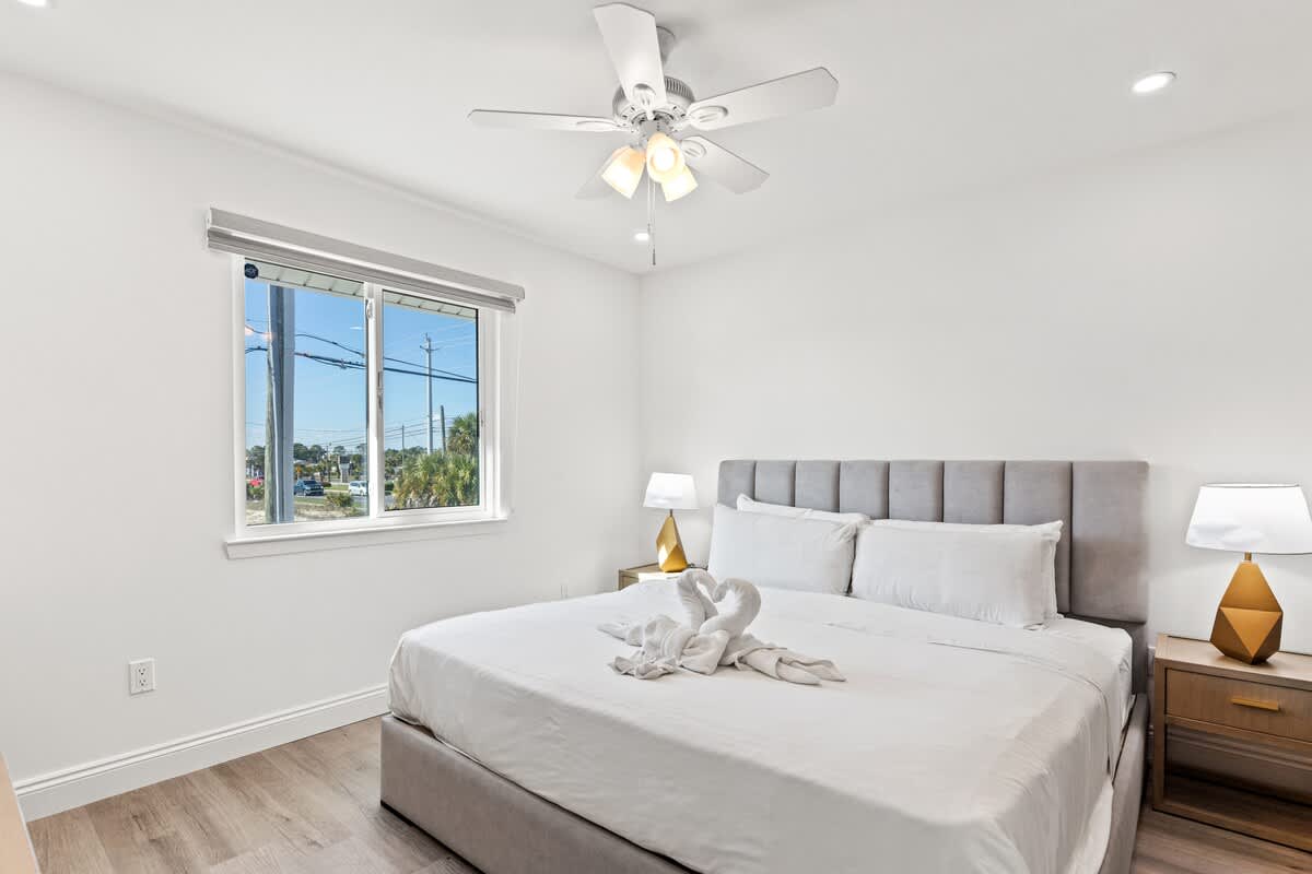 Ocean Breeze 2C – Bright bedroom with a queen bed, window view, ceiling fan, and nightstands.