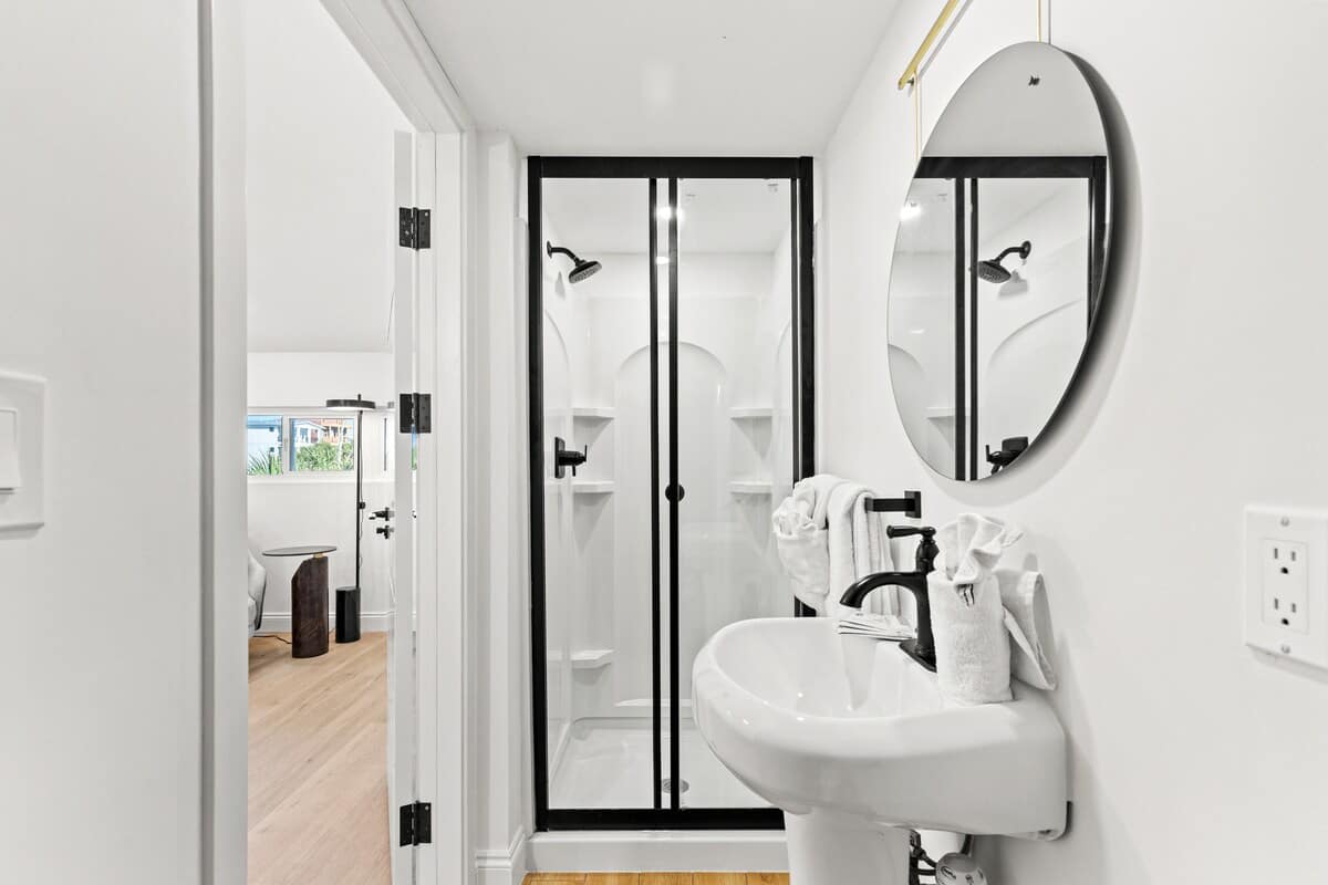 Ocean Breeze 2C – Bathroom with a shower, round mirror, and sink; wooden floor visible.
