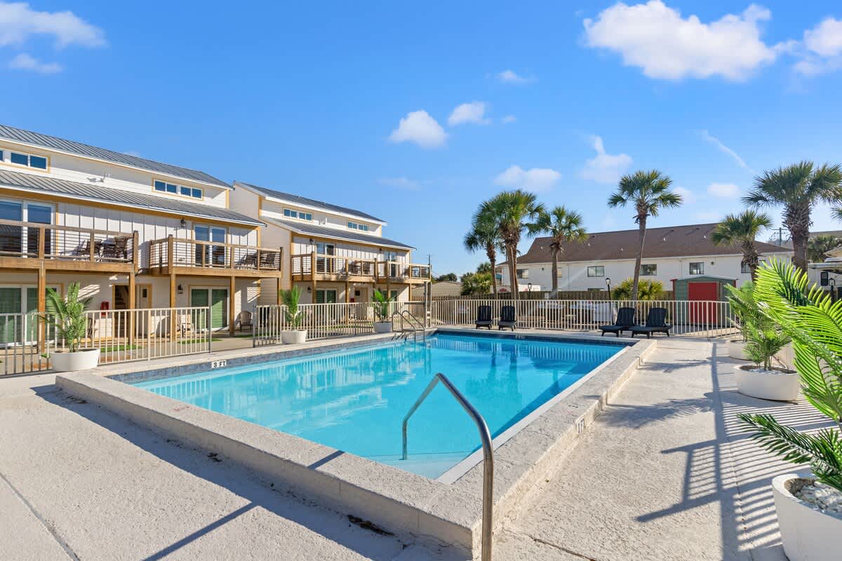 Ocean Breeze 2C – Swimming pool surrounded by palm trees and vacation rental units with balconies. Clear blue sky above.
