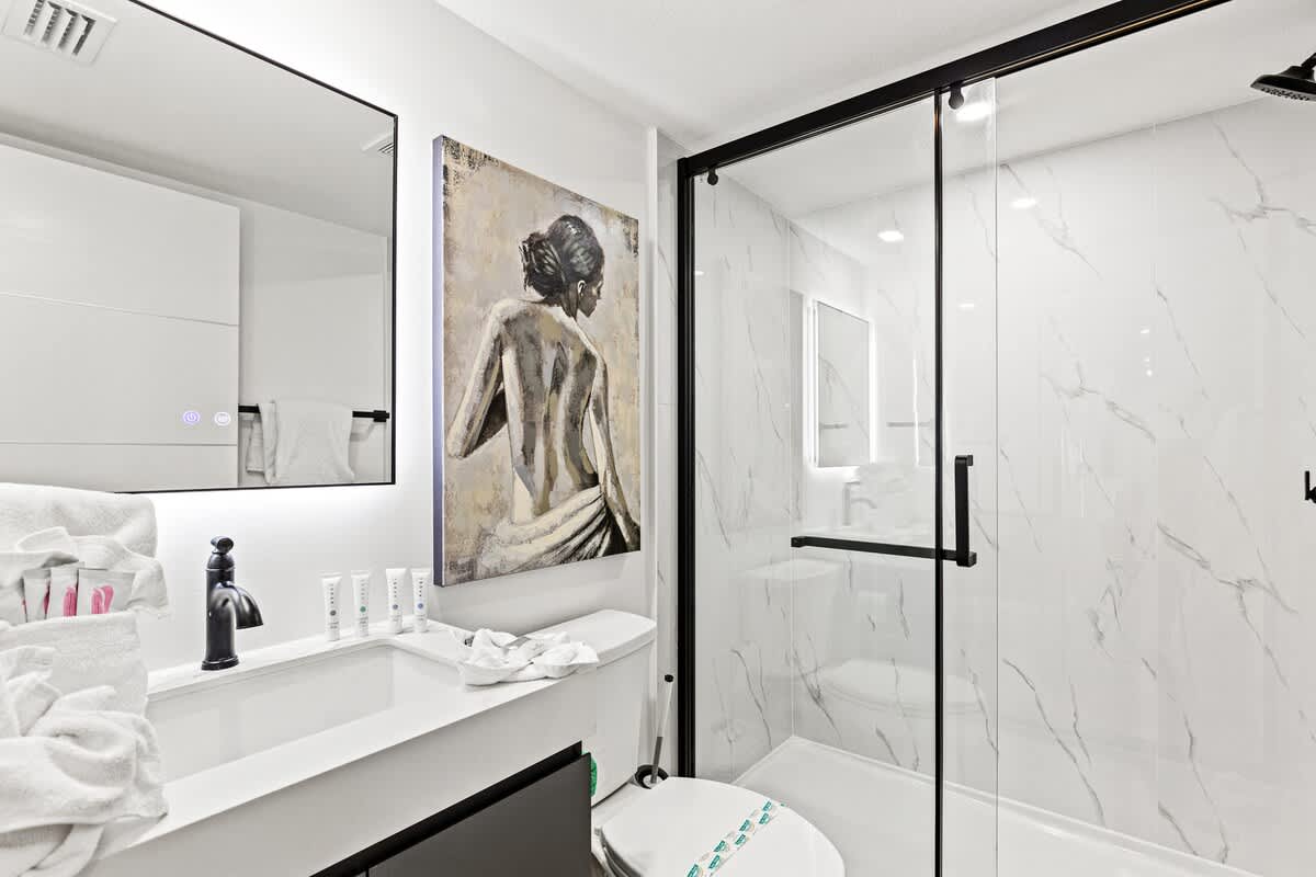 Ocean Breeze 2C – Modern bathroom with glass shower, marble tiles, a large mirror, and decorative wall art.