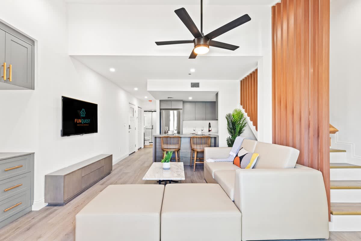 Ocean Breeze 2C – Modern living area with beige sofa, coffee table, kitchen bar, and stairway in a vacation rental.