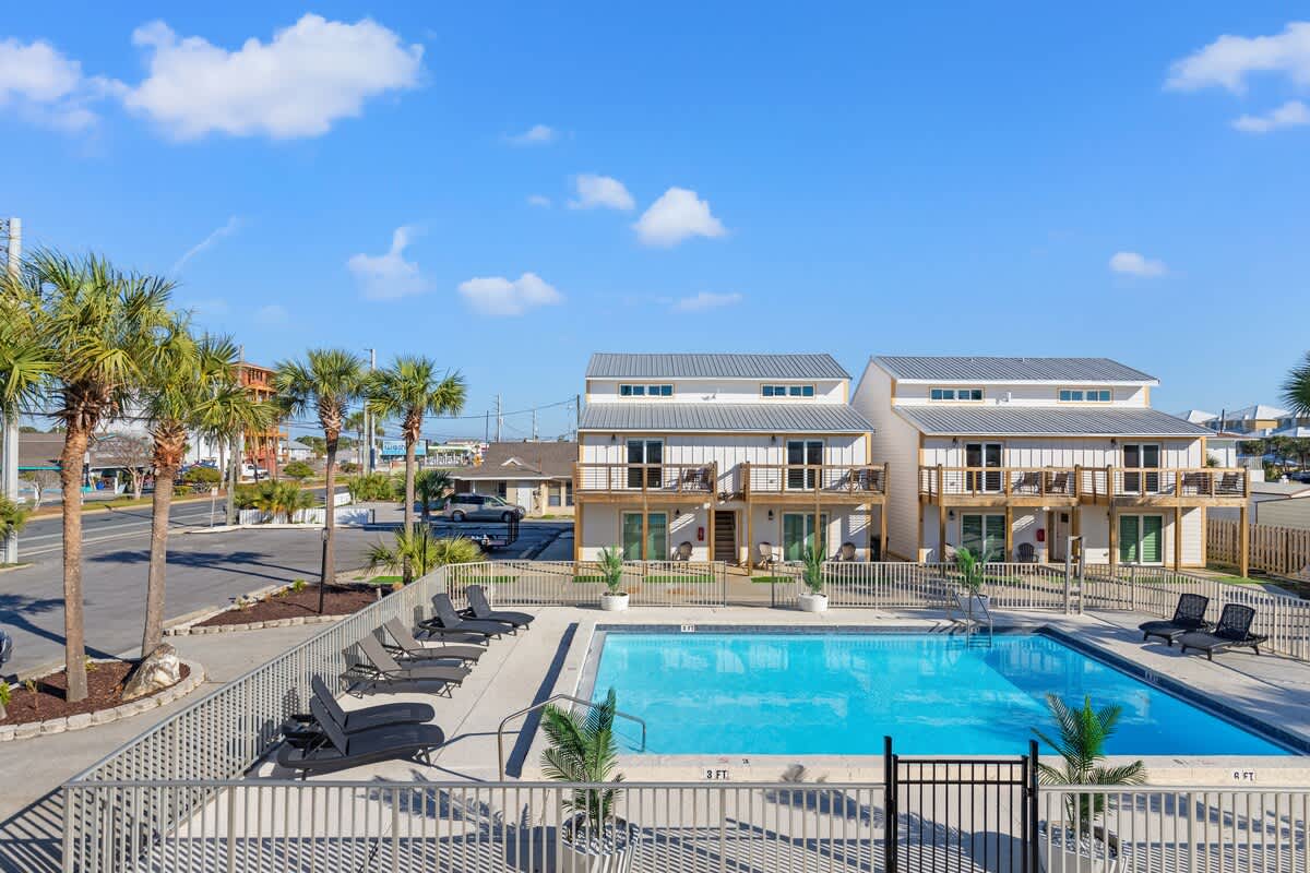 Ocean Breeze 2C – Two-story vacation rental units with balconies, pool area, palm trees, and clear blue sky.