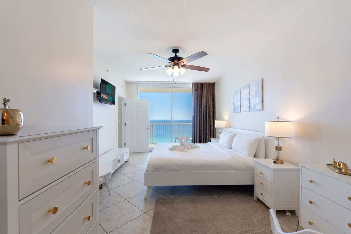 Majestic T2 - 1606 – Bright bedroom with a king-size bed, oceanview balcony, dresser, and two bedside lamps.