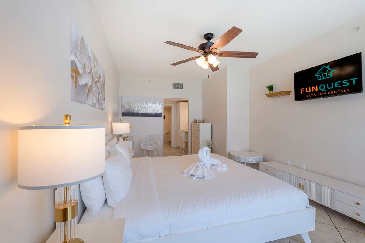 Majestic T2 - 1606 – Bright bedroom featuring a king bed, ceiling fan, two lamps, and a TV on the wall.