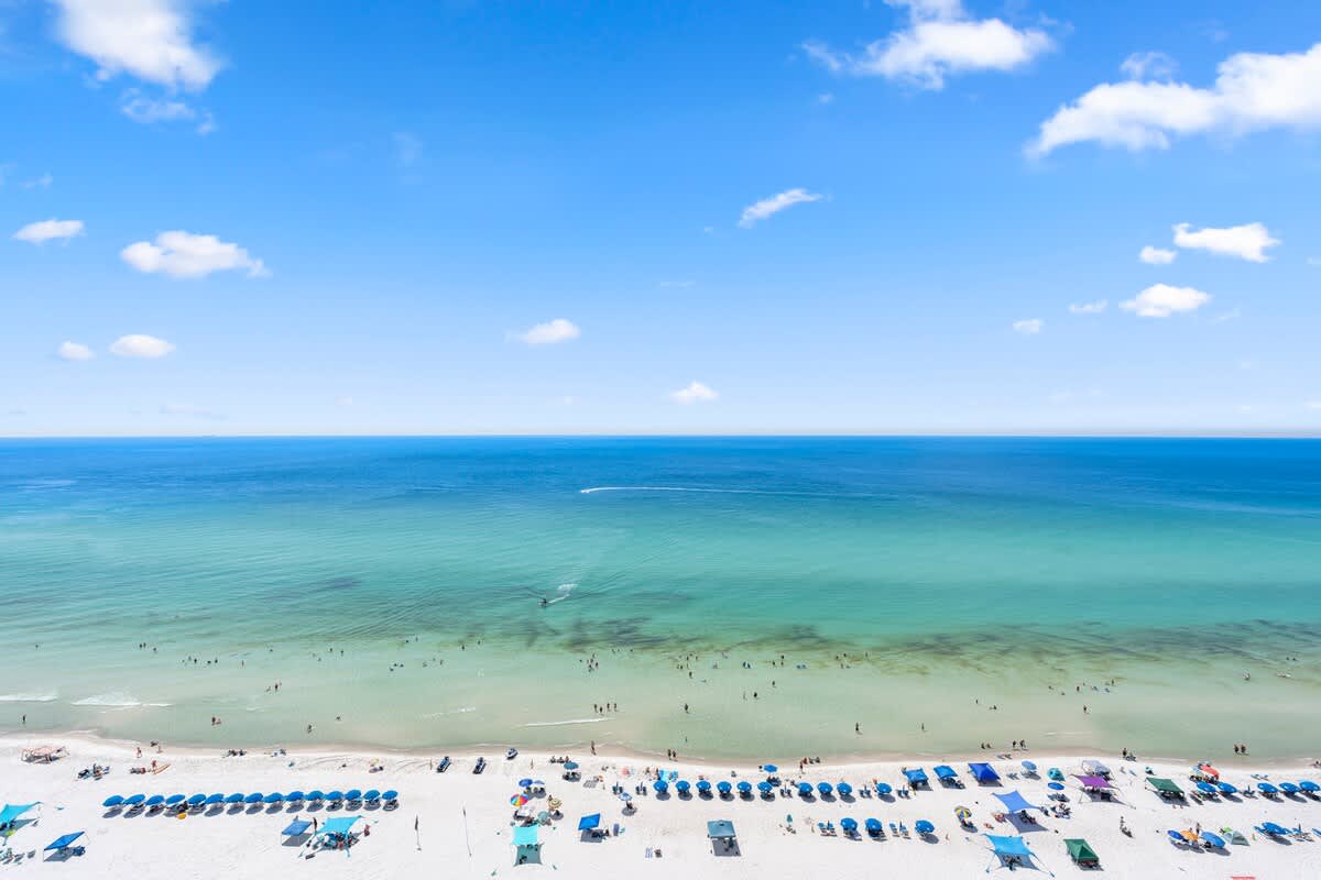 Majestic T2 - 1606 – Aerial view of a beach with sunbeds, a clear sea, and people enjoying the water.